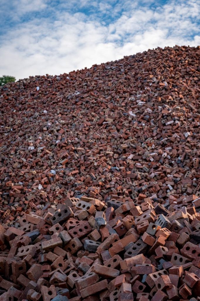 A large heap of irregularly piled, used red bricks under a partly cloudy sky, showcasing construction waste.